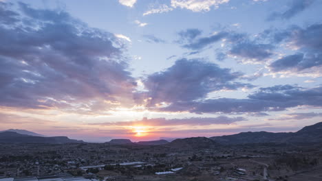 Hyperlapse-of-a-cloudy-sunset,-sun-sets-behind-the-mountains-on-the-horizon,-in-the-center-of-the-frame