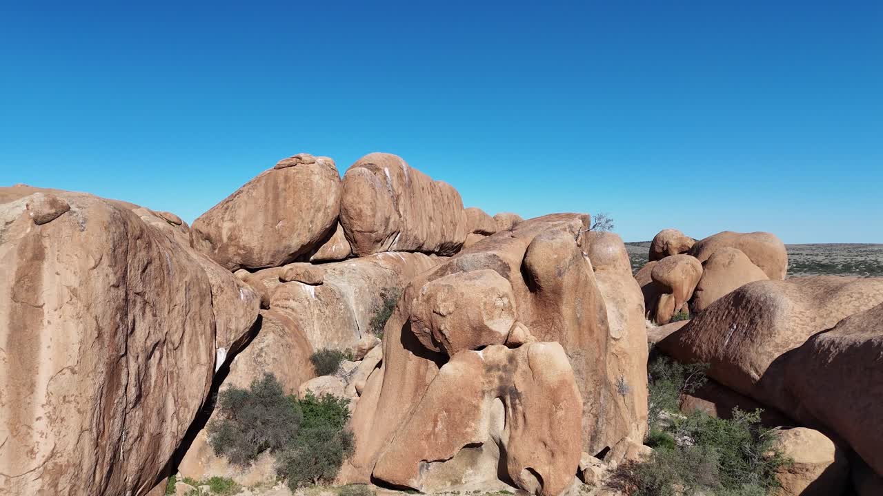 massive red granite boulders at Spitzkoppe, surrounded by dry savanna vegetation and the open Namibian desert under clear skies