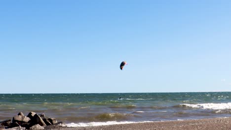 a lone kiteboarder skillfully traversing a rocky shoreline, on a beautify, virtually cloudless day