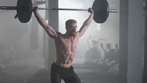 slow motion: brutal athlete lifts the bar above himself performing a jerk a spinning push. a man is engaged in weightlifting on a dark background portrait. concept strength power playing sports.