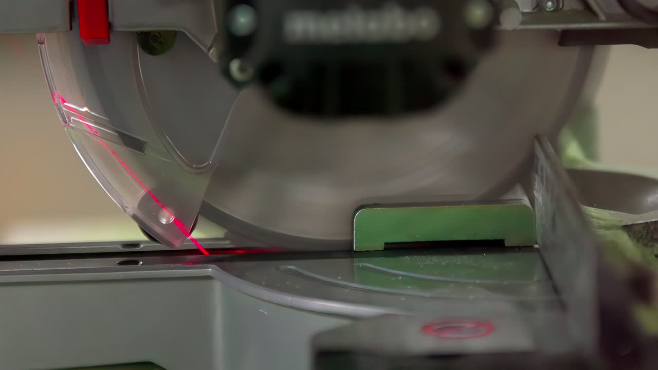 Gros plan d'une scie à onglet avec guide laser coupant un matériau au ralenti. La lame circulaire en rotation et l'alignement de précision mettent en évidence un travail de menuiserie professionnel.