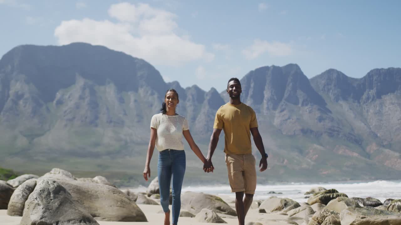 pareja afroamericana cogida de las manos y caminando por la playa
