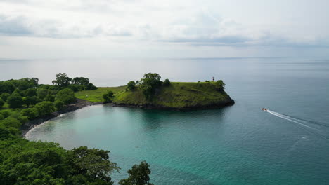 Drone-shot-of-a-boats-driving-past-the-Lagoa-Azul-lighthouse,-in-Sao-Tome,-Africa