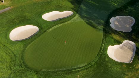 Inclinación-Aérea-Hacia-Abajo-Del-Campo-De-Golf-Verde,-Trampas-De-Arena-Durante-La-Hermosa-Luz-De-La-Mañana