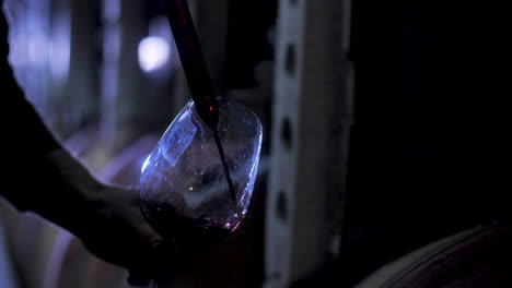 a worker of a winery pouring red wine into a glass with a syringe