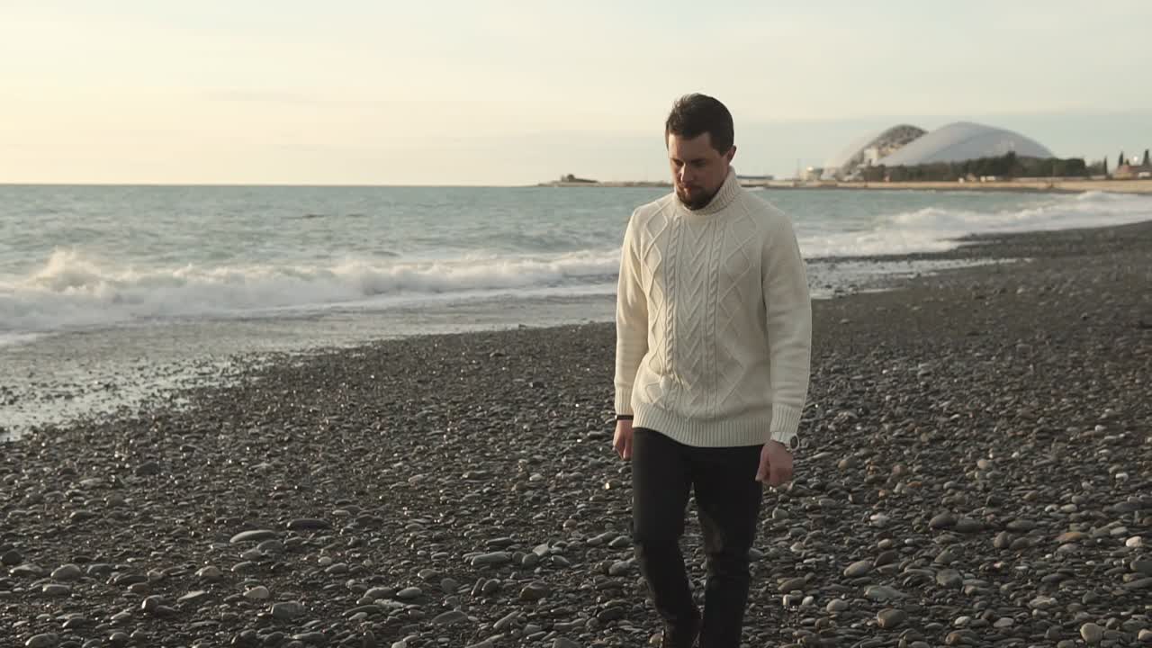 hombre caminando por una playa de guijarros durante el atardecer