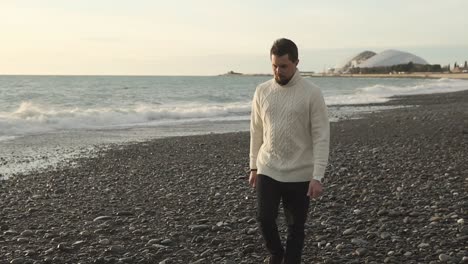 man walking on a pebble beach during sunset