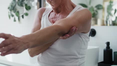 unrecognizable senior woman applying moisturizing cream on arms