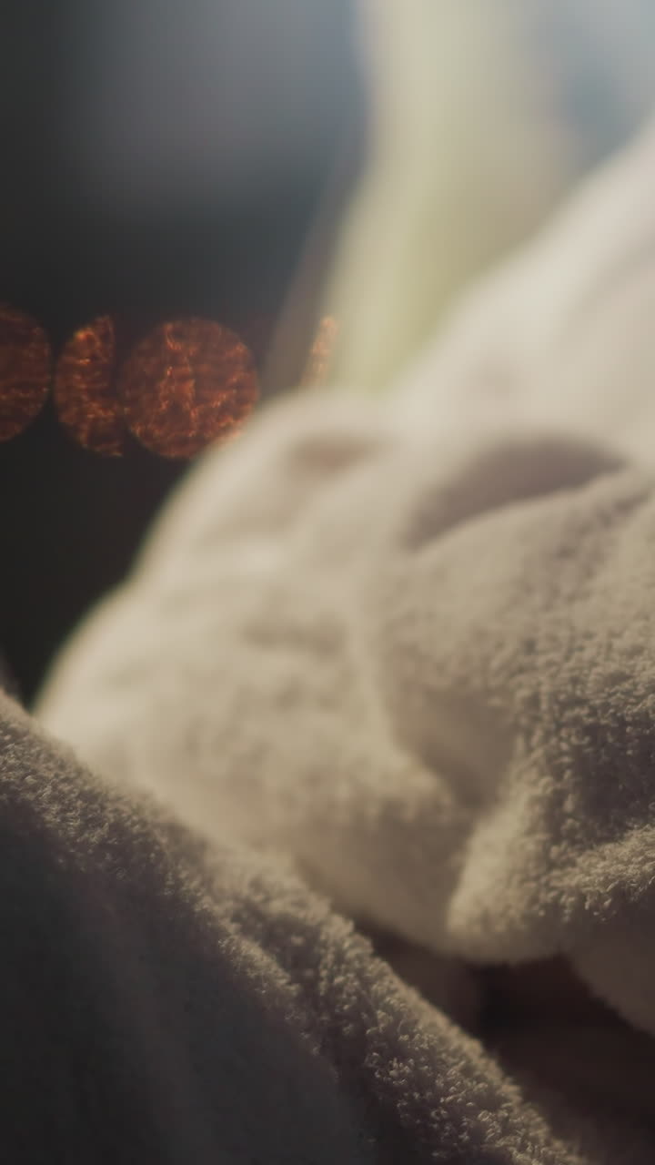 테리 목욕복을 입은 여성은 창문에 맞춰 의자에 앉아 야간 생활 환경을 바라보고 있습니다. 여자는 휴식을 취하고 아파트에서 느린 동작의 전망을 즐기고 있습니다.