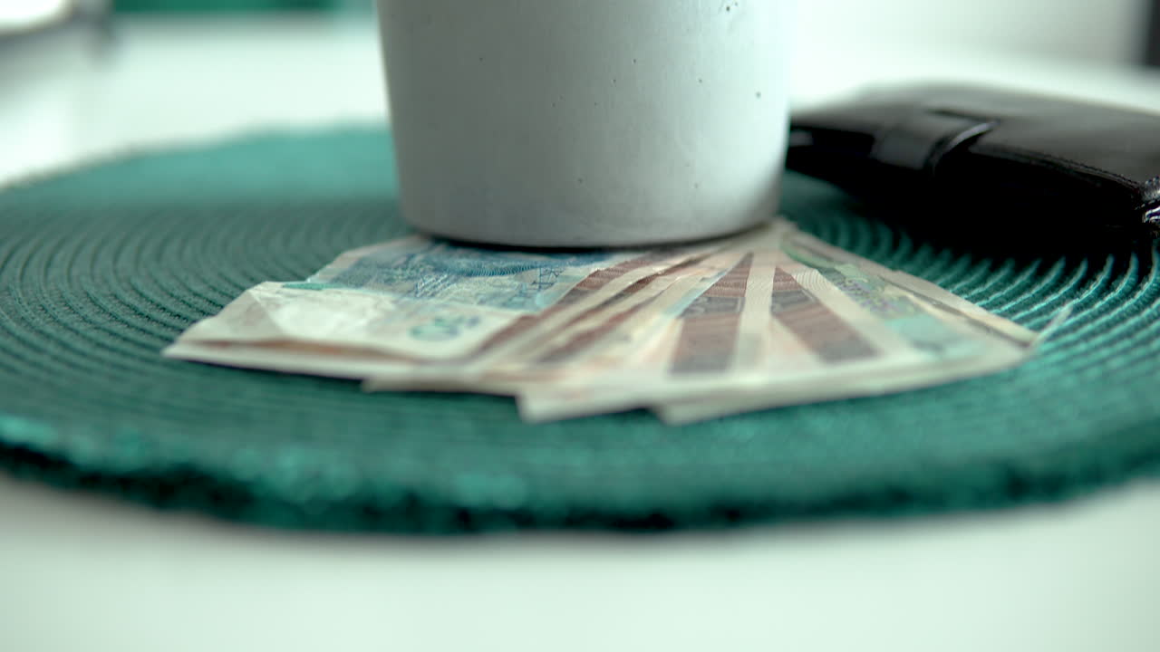Ciemne ujęcie z góry stosu banknotów i portfela z pieniędzmi pod rośliną doniczkową.