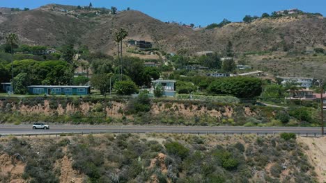 wide aerial drone shot tracking cars parallel to the highway on the hills of malibu coastline in california during a hot summer day in the usa