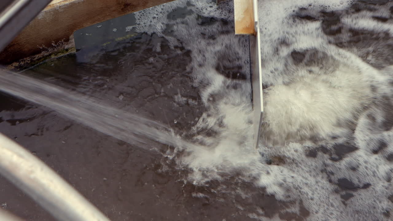 Water enters the clarifying pond at a wastewater treatment plant, slowly flowing and mixing as sediments settle, beginning the industrial purification process