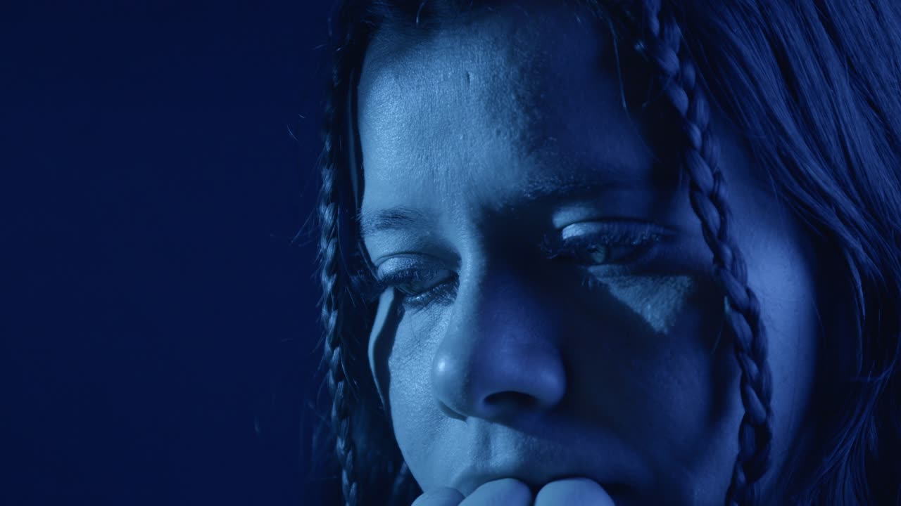 A close-up shot of a girl appearing confused, hands on her face, bathed in deep blue moody lighting. Emotional depth and dramatic tone highlight her expression
