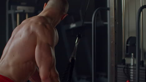 bodybuilding concept. muscular man doing cable rope triceps pull down exercise while working out in gym