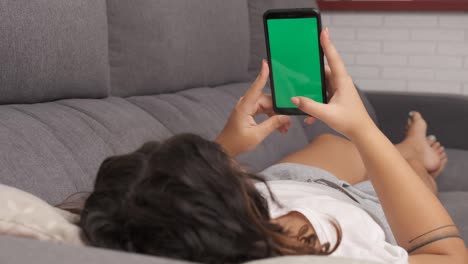 mujer en el sofá de la sala de estar viendo algo en su teléfono celular, pantalla verde en el teléfono inteligente