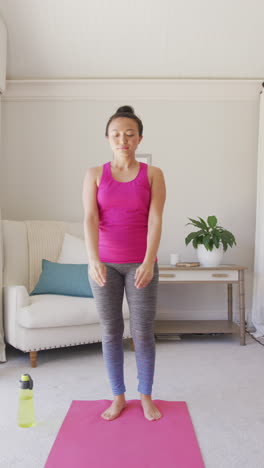 vertical video of happy asian woman doing yoga and stretching in bedroom, in slow motion