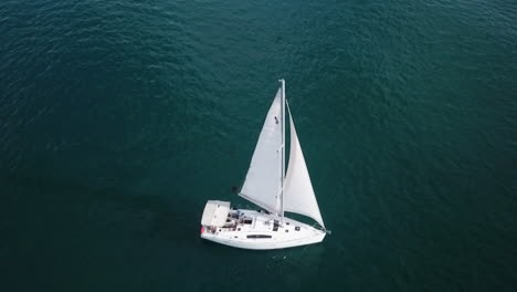 top view aerial footage of white yacht sailing slowly in calm blue seas