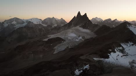 Sobrevuelo-Aéreo-Sobre-El-Glaciar-De-Vouasson-Cerca-De-Arolla-En-Valais,-Suiza-Al-Atardecer-Con-Un-Colorido-Resplandor-Detrás-De-Las-Aiguilles-Rouges,-El-Mont-Blanc-De-Cheillon,-El-Grand-Combin-Y-Otros-Picos