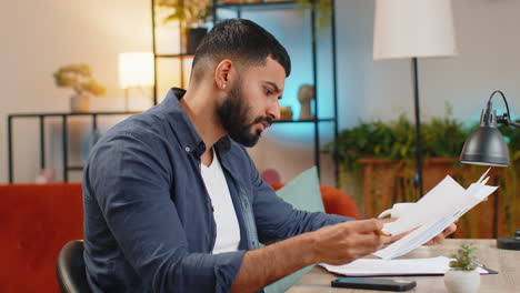 hombre indio freelance trabajando con documentos desde la oficina de casa analizando la lectura de informes de negocios