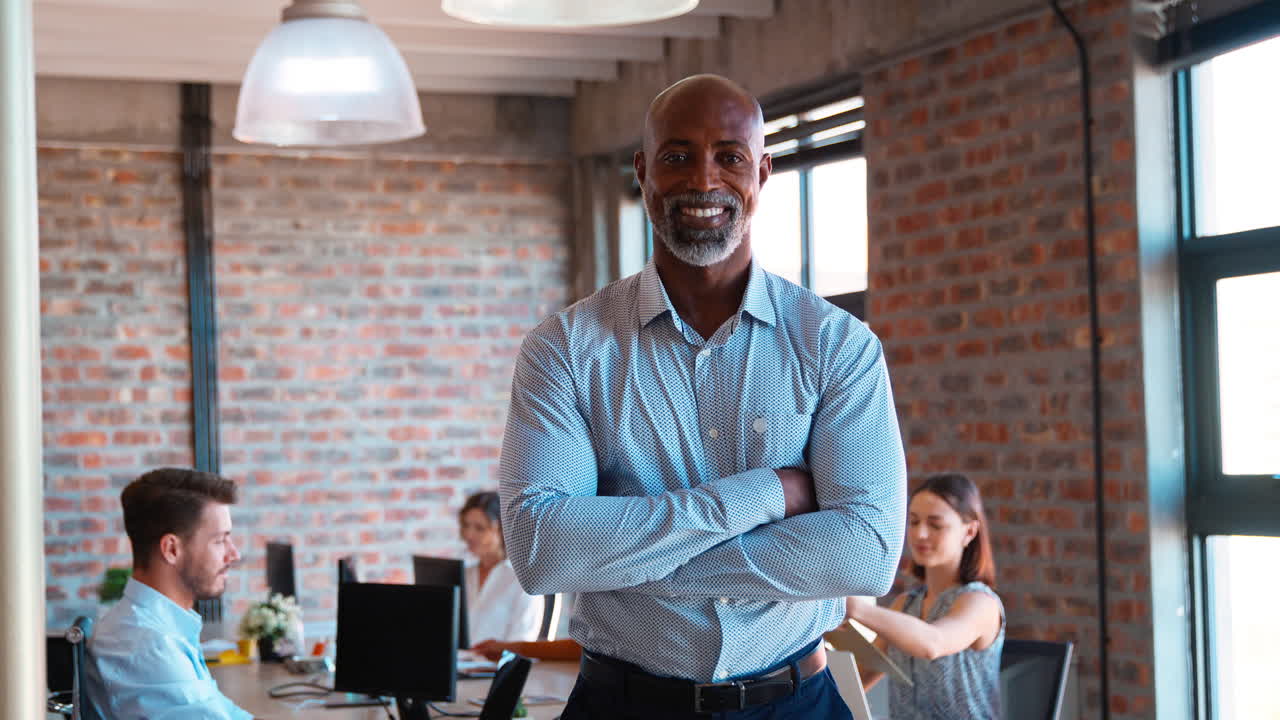 retrato de un hombre de negocios maduro sonriente de pie en una oficina ocupada con colegas trabajando en el fondo