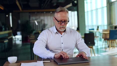businessman arranging his working place in the office. man in glasses sits at opening his laptop and moving gadget and paper notebook.