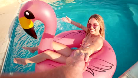 Young woman floating on inflatable flamingo splashing boyfriend with water