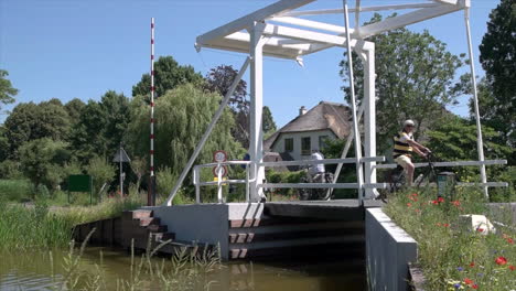 adult men biking and crossing bridge over stream in reeuwijkse plassen on a sunny day in netherlands