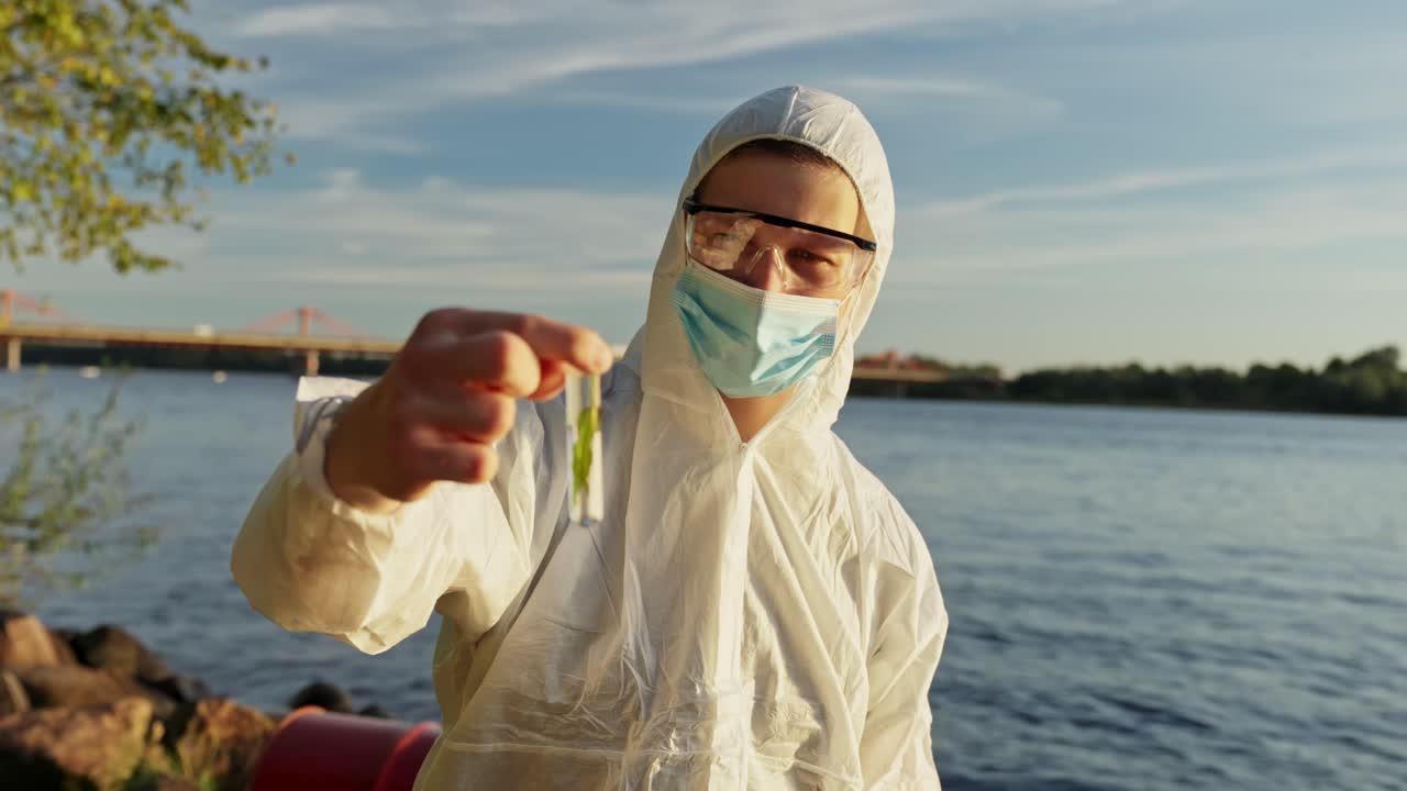 Giovane ispettore ambientale in tuta protettiva che raccoglie campioni d'acqua da un fiume inquinato, analizzandone la contaminazione e monitorando la salute ecologica sotto un cielo sereno