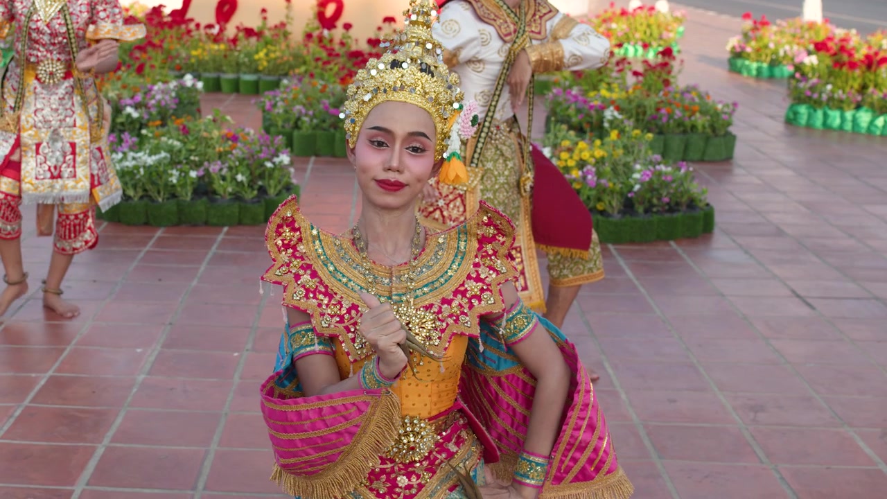 Thailandske dansere i udsmykkede guldkostumer udfører klassiske Manohra-bevægelser udendørs ved et historisk tempel.