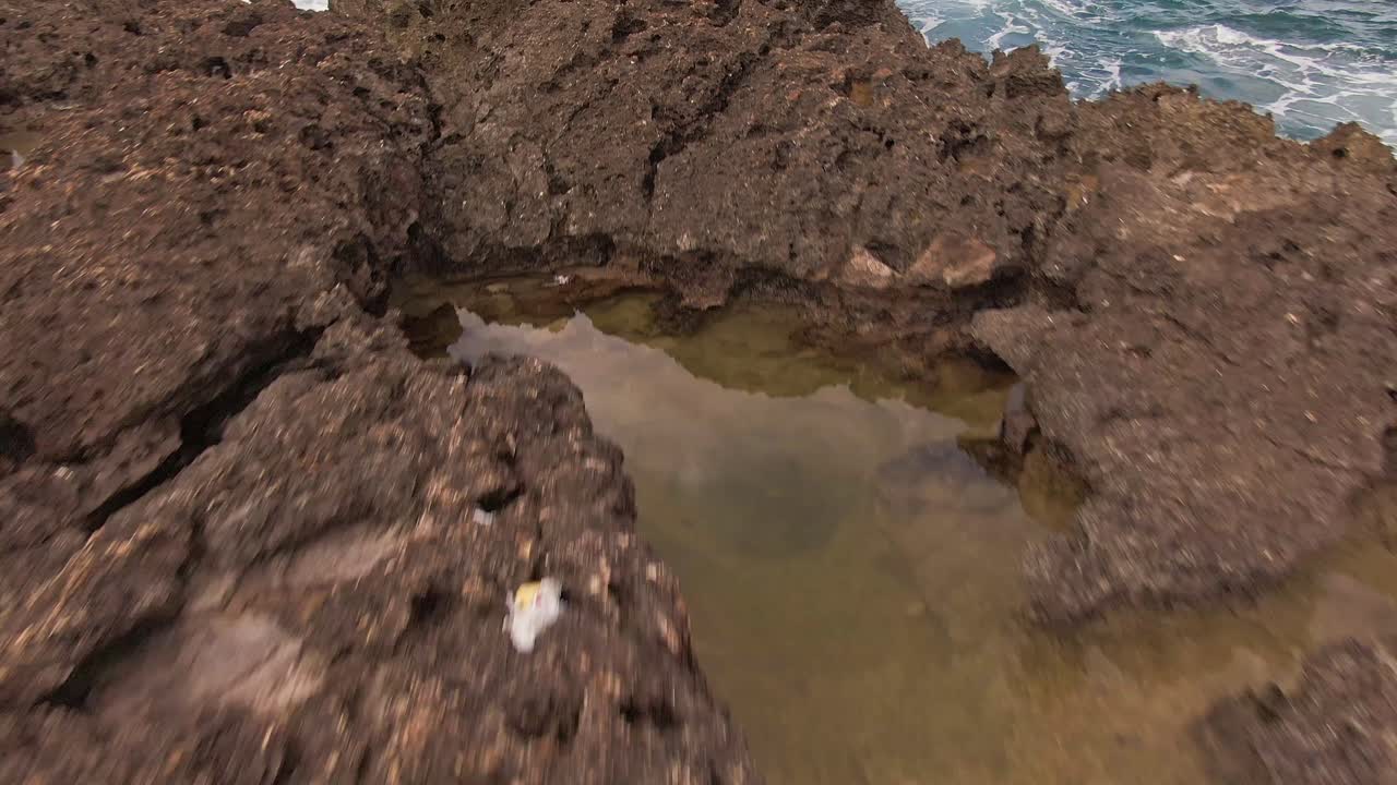 Carrellata in avanti con angolazione bassa di una formazione rocciosa su una spiaggia hawaiana