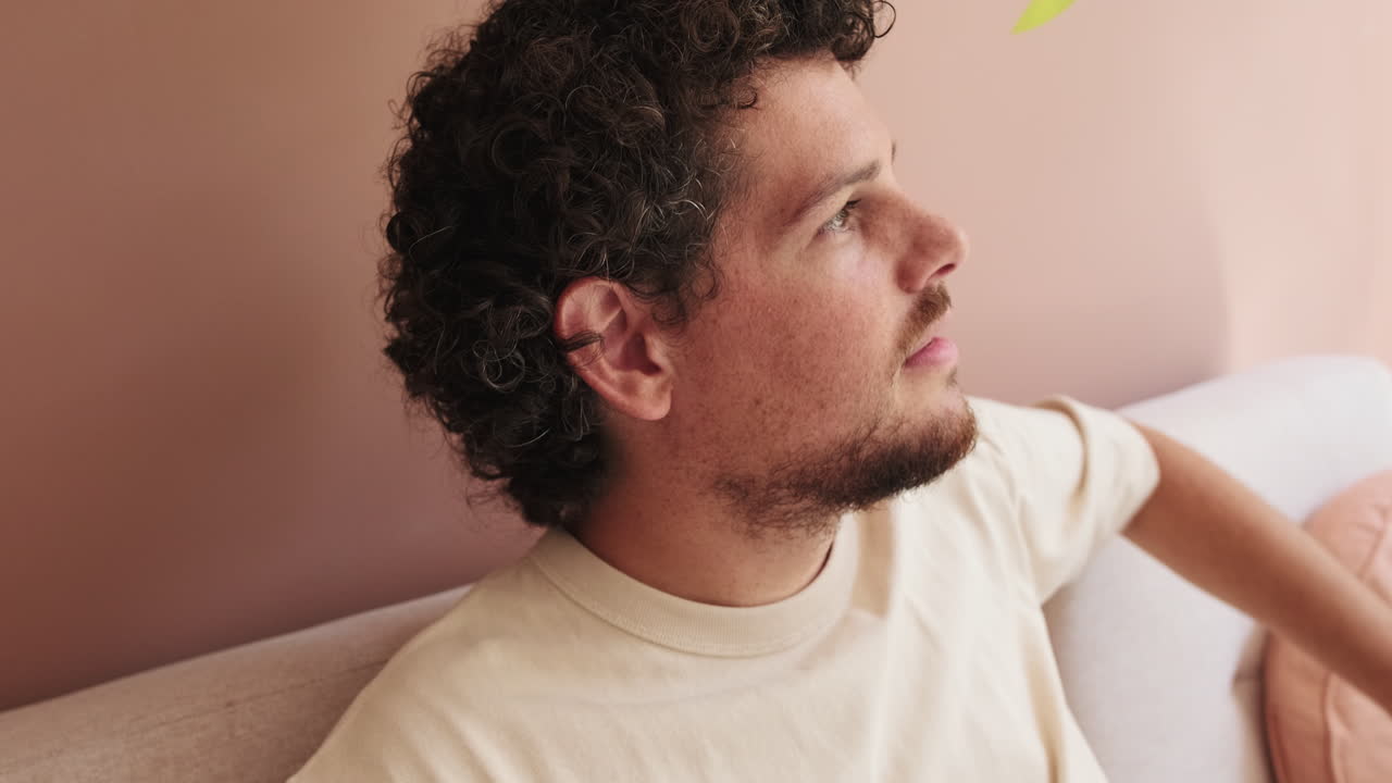 Profile of Thoughtful Man with Curly Hair Sitting on Sofa