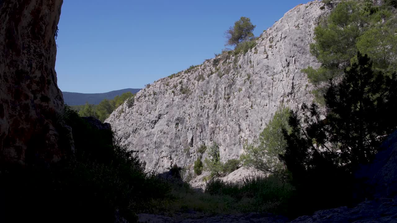 silueta de la boca de la cueva con arbustos contra un acantilado de roca iluminado por el sol, españa