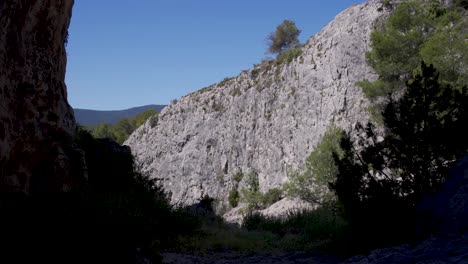 silhouette of cave mouth with bushes against a sunlit rock cliff,spain