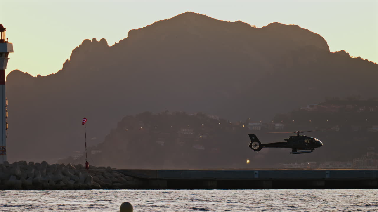 View of a helicopter landing at sunset near a lighthouse with the mountains on the background in the south of France
