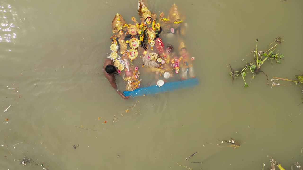 Aerial shot of poor man taking idol of Hindu Goddess Durga for immersion in ganga river, garbage polluting river water