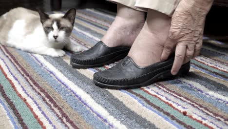 mujer anciana con los pies hinchados se pone zapatos en casa
