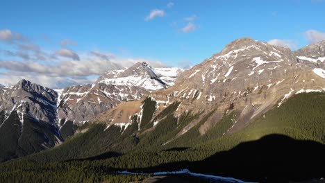 Vista-Aérea-épica-De-Una-Cresta-De-Montaña-Con-Nieve-En-La-Parte-Superior-Y-Un-Bosque-De-árboles-Alpinos-Verdes-En-Primer-Plano-En-Un-Día-Soleado,-Toma-Amplia,-Concepto-De-Conservación