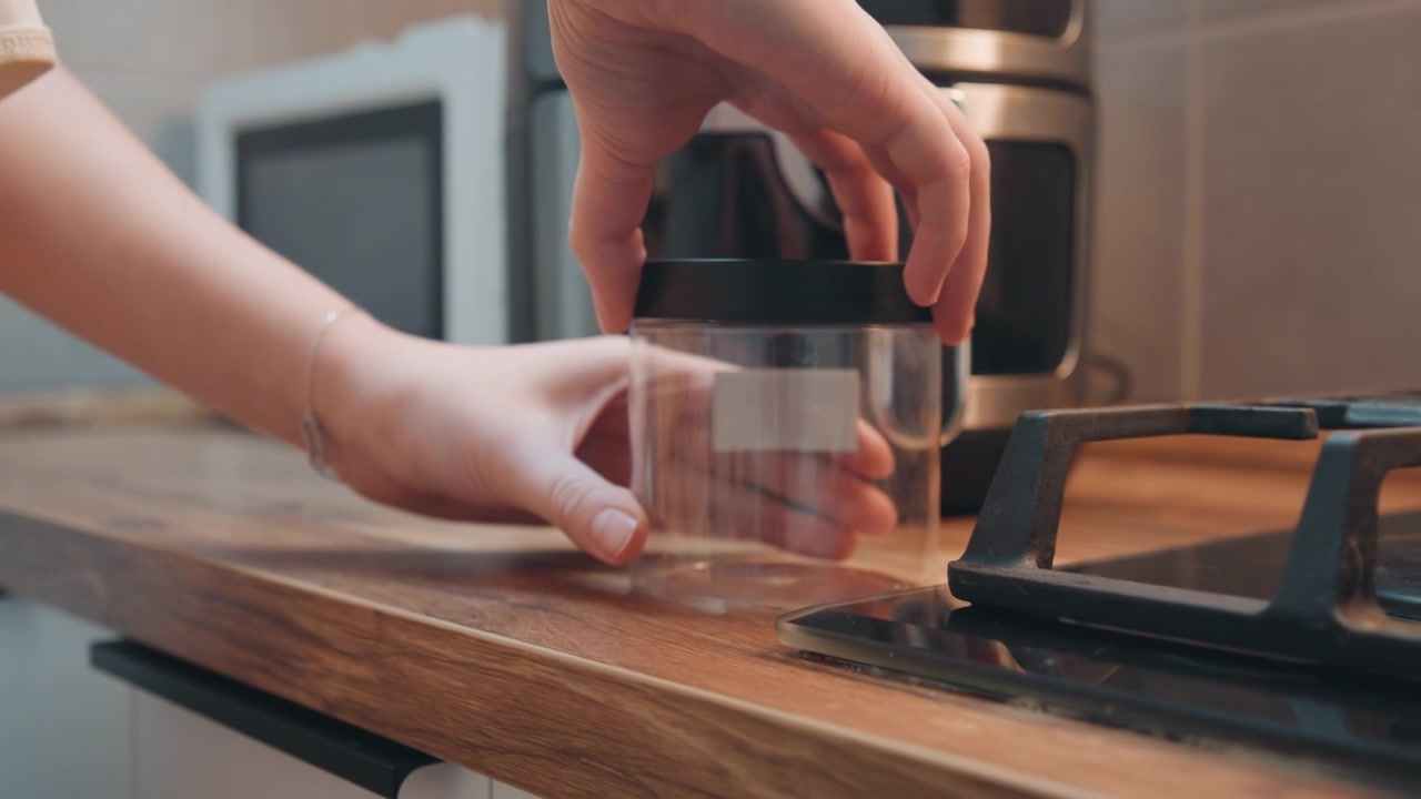 Cooking with glass lid. Chef handles transparent container cautiously. Preparing meal using glass covering on counter. Chef carefully manages clear glass container during cooking process