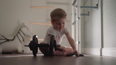 focused little boy puts plates on barbell sitting on floor