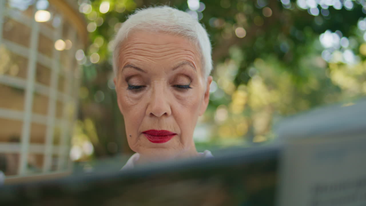 Retired woman reading newspaper in city park portrait. Focused stylish lady