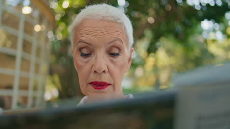 retired woman reading newspaper in city park portrait. focused stylish lady