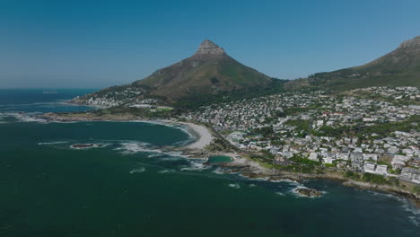 Panoramaaufnahmen-Aus-Der-Luft-Des-Reiseziels.-Wohnbezirk-An-Der-Küste-Mit-Strand-In-Der-Bucht-An-Einem-Sonnigen-Tag.-Hoher-Berggipfel-Im-Hintergrund.-Kapstadt,-Süd-Afrika