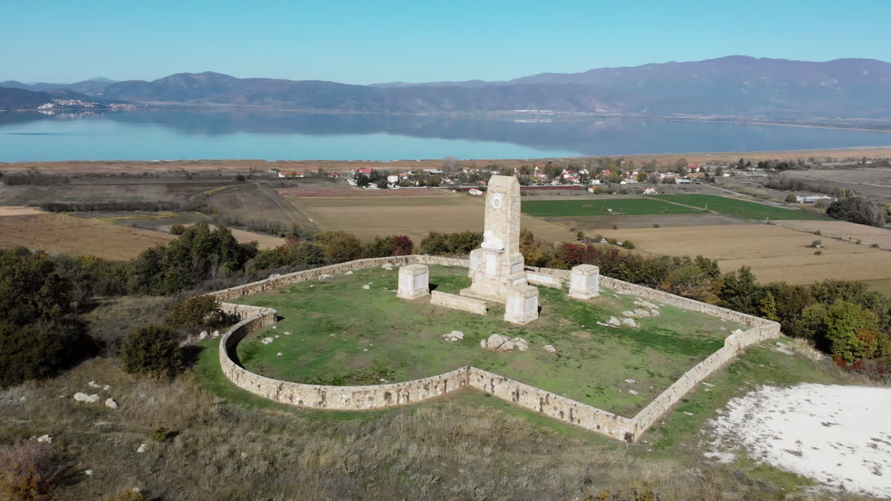 Güneşli bir günde, Doyran Gölü'ne bakan, üzerinde aslan heykeli bulunan Doyran Anıtı ve Askeri Mezarlığı'nın ve ötesindeki kırsal dağ manzarasının drone çekimi.