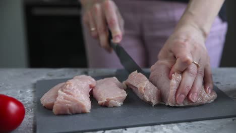 mujer cortando pecho de pollo crudo en una tabla de cortar