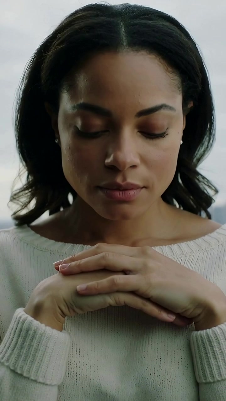 Vertical video: Lowering gaze woman in cream sweater folding hands under chin at window, reflecting