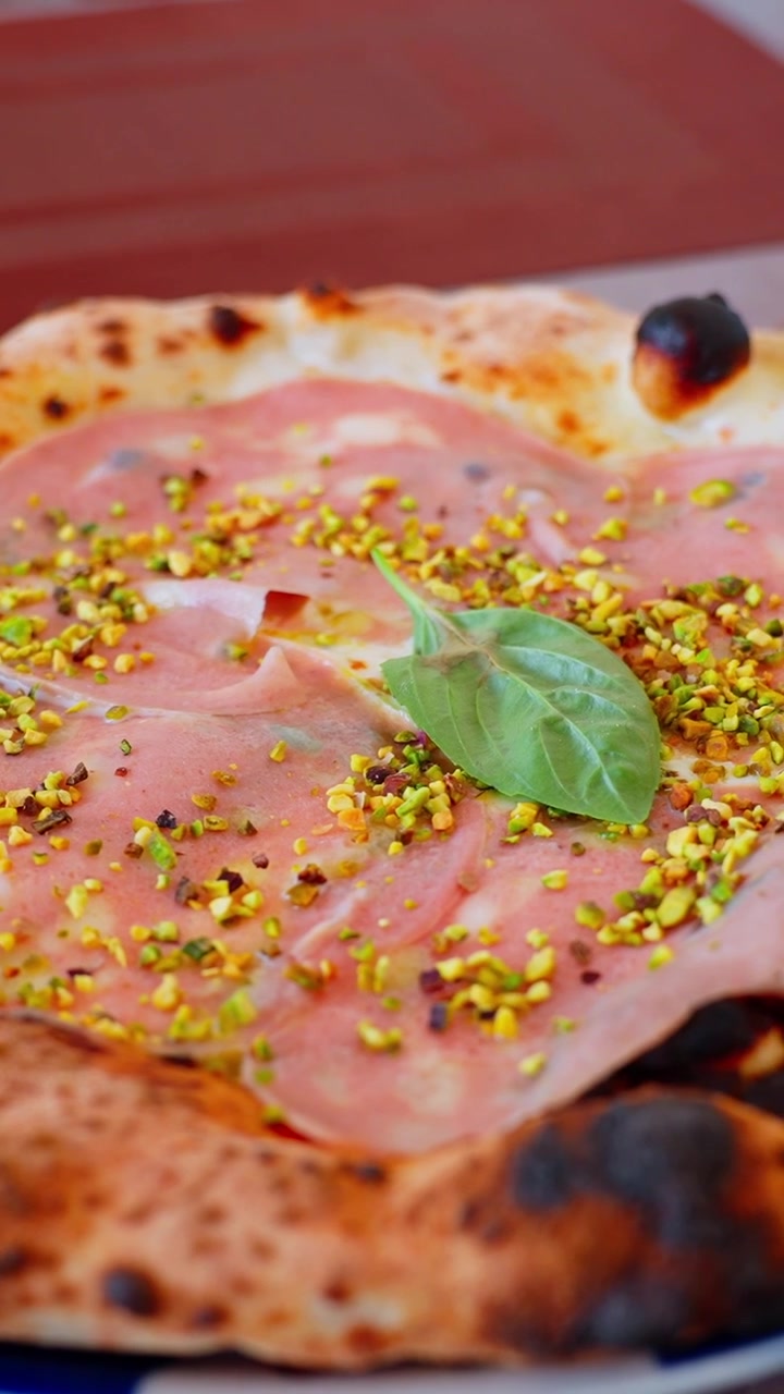 Primo piano verticale di pizza con mortadella e pistacchio, con basilico su un cornicione a bolle, che cattura il cibo artigianale italiano con ricchi dettagli da ristorante