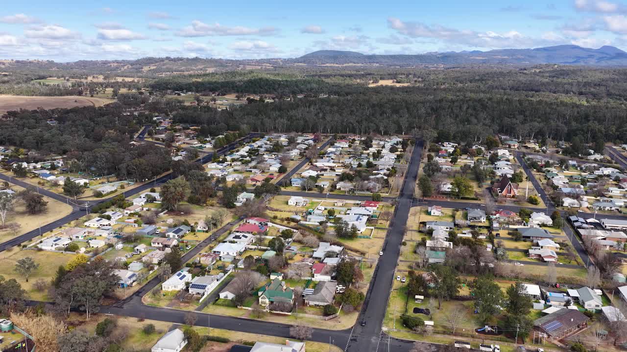 Drone footage glides above a suburban neighborhood in Coonabarabran, New South Wales, revealing houses, gardens, and streets under bright daylight with steady camera movement