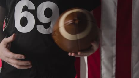 Close-Up-Of-American-Football-Player-Holding-Ball-Against-Stars-And-Stripes-Flag-In-Background-1