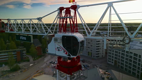 The-cabinet-of-a-flat-top-construction-crane-in-sunset,-forest-and-buildings-in-the-background