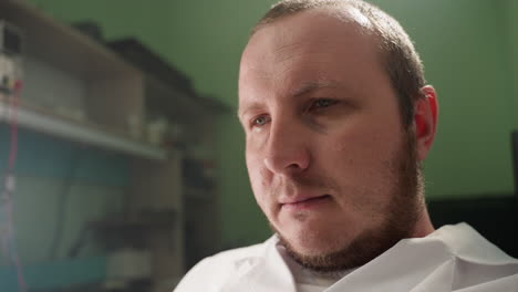 a close-up view of a technician in a white lab coat looking focused and thoughtful in a laboratory, the background shows shelves with lab equipment